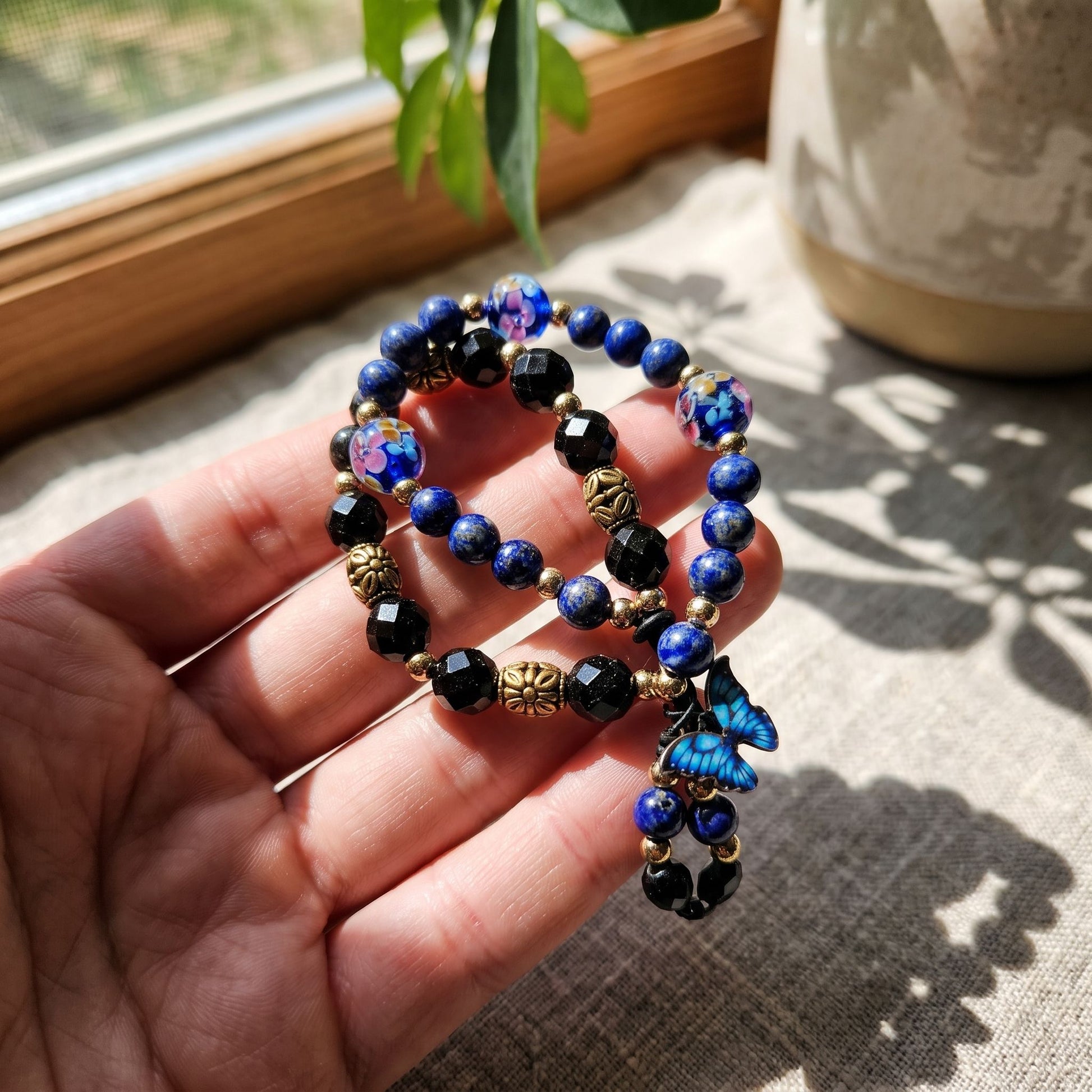 Blue Lapis bracelet held on fingertips near a sunlit window, highlighting crystal sparkle.