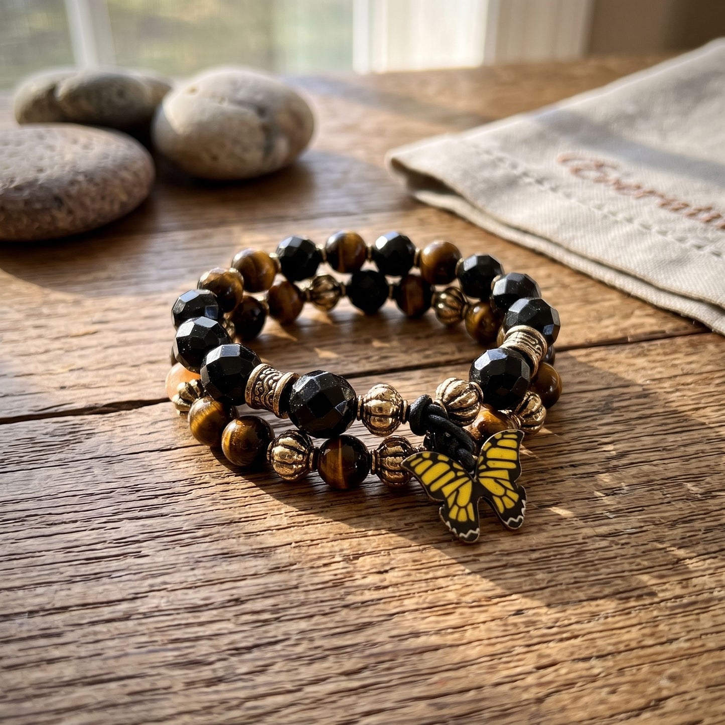 Close-up of delicate Golden Tiger Eye Dual Crystal Energy bracelet with butterfly clasp on wooden surface, illuminated by warm sunlight.