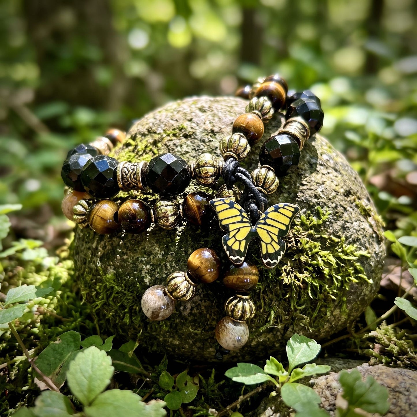 Natural outdoor shot of tiny Golden Tiger Eye Dual Crystal Energy bracelet over moss-covered stone surrounded by greenery, earthy and grounding.