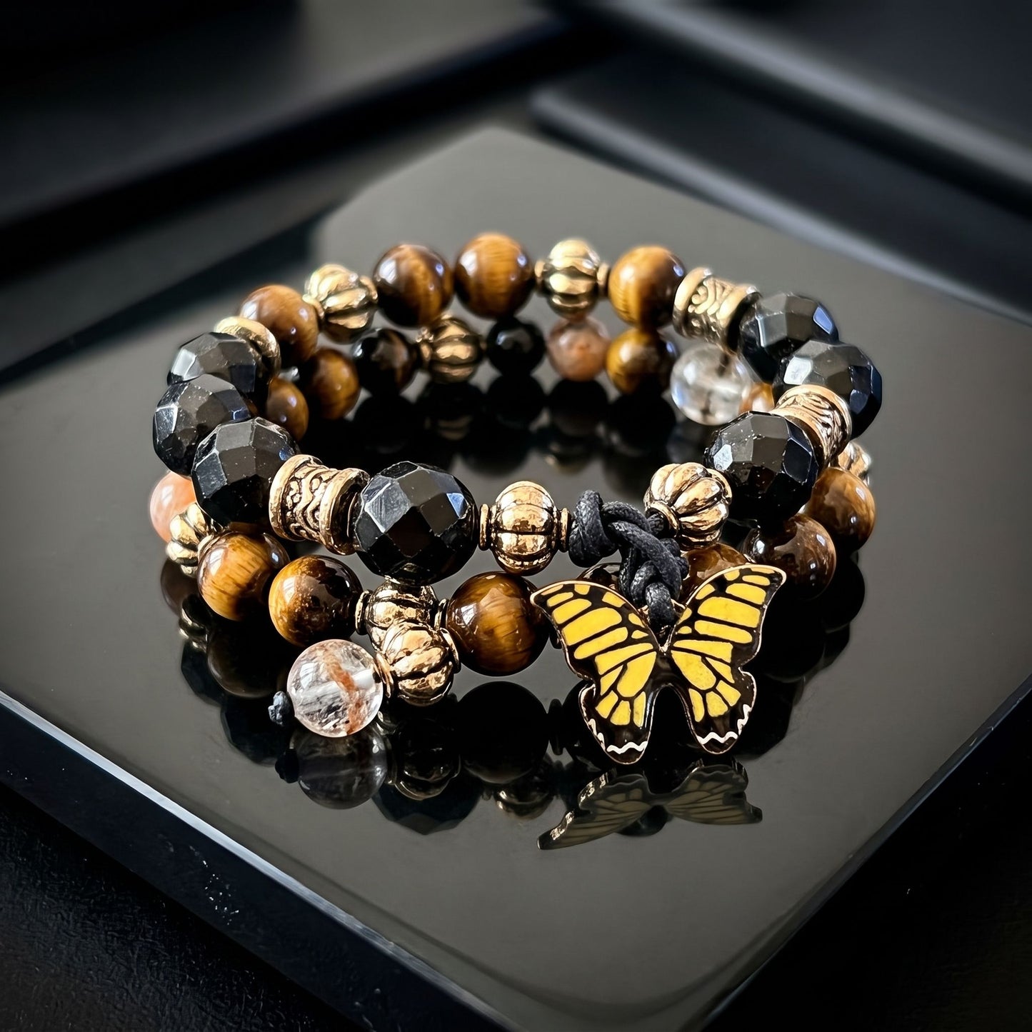 Professional image of delicate Golden Tiger Eye Dual Crystal Energy bracelet on black reflective surface, emphasizing craftsmanship and materials.